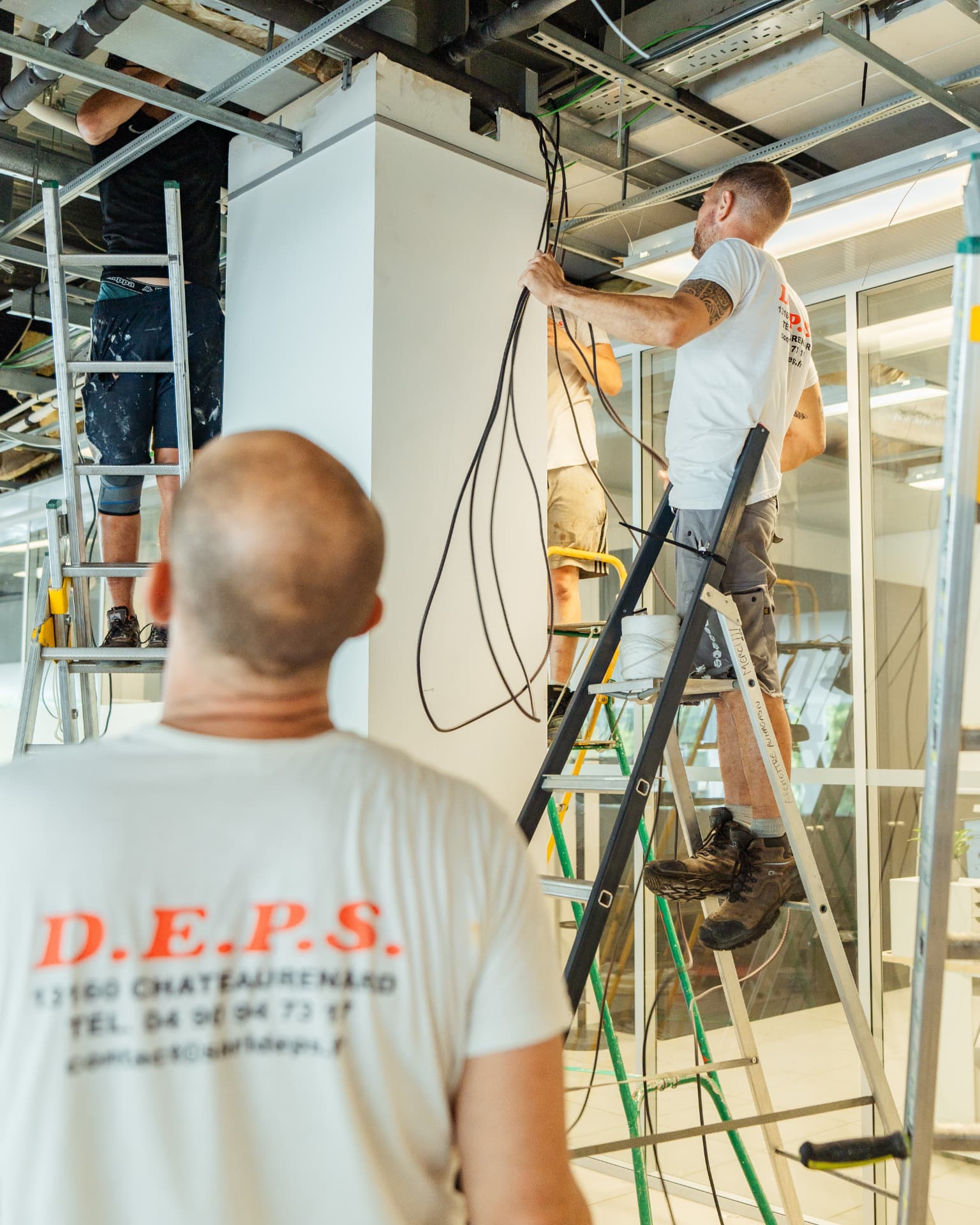 Équipe d'une entreprise du bâtiment au travail sur un chantier, deux compagnons sur des échelles tirant des câbles au plafond