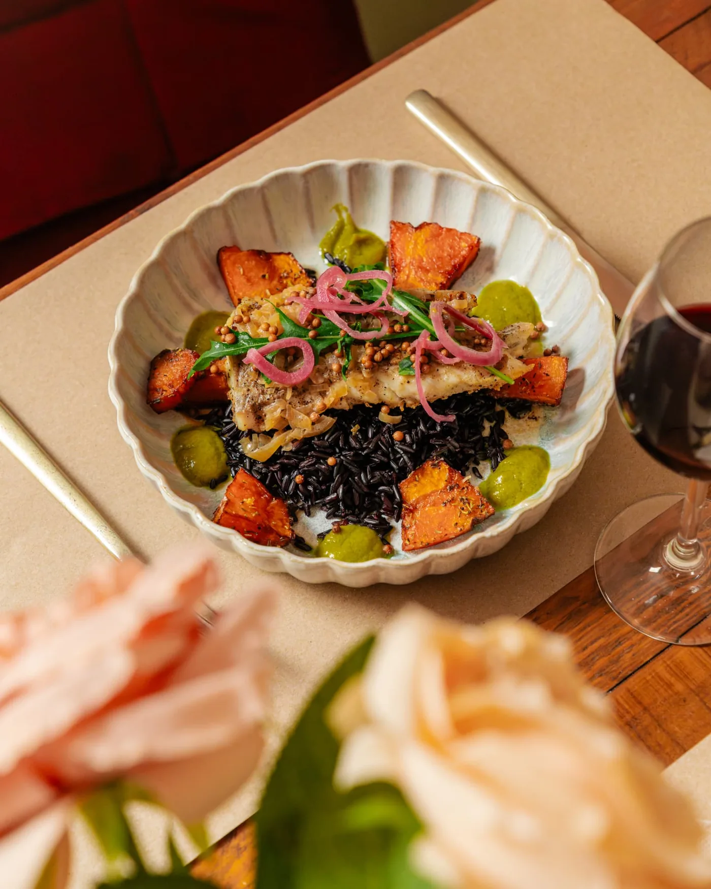 Assiette de poisson, riz noir et légumes rôtis photographiée en lumière naturelle sur une table de restaurant
