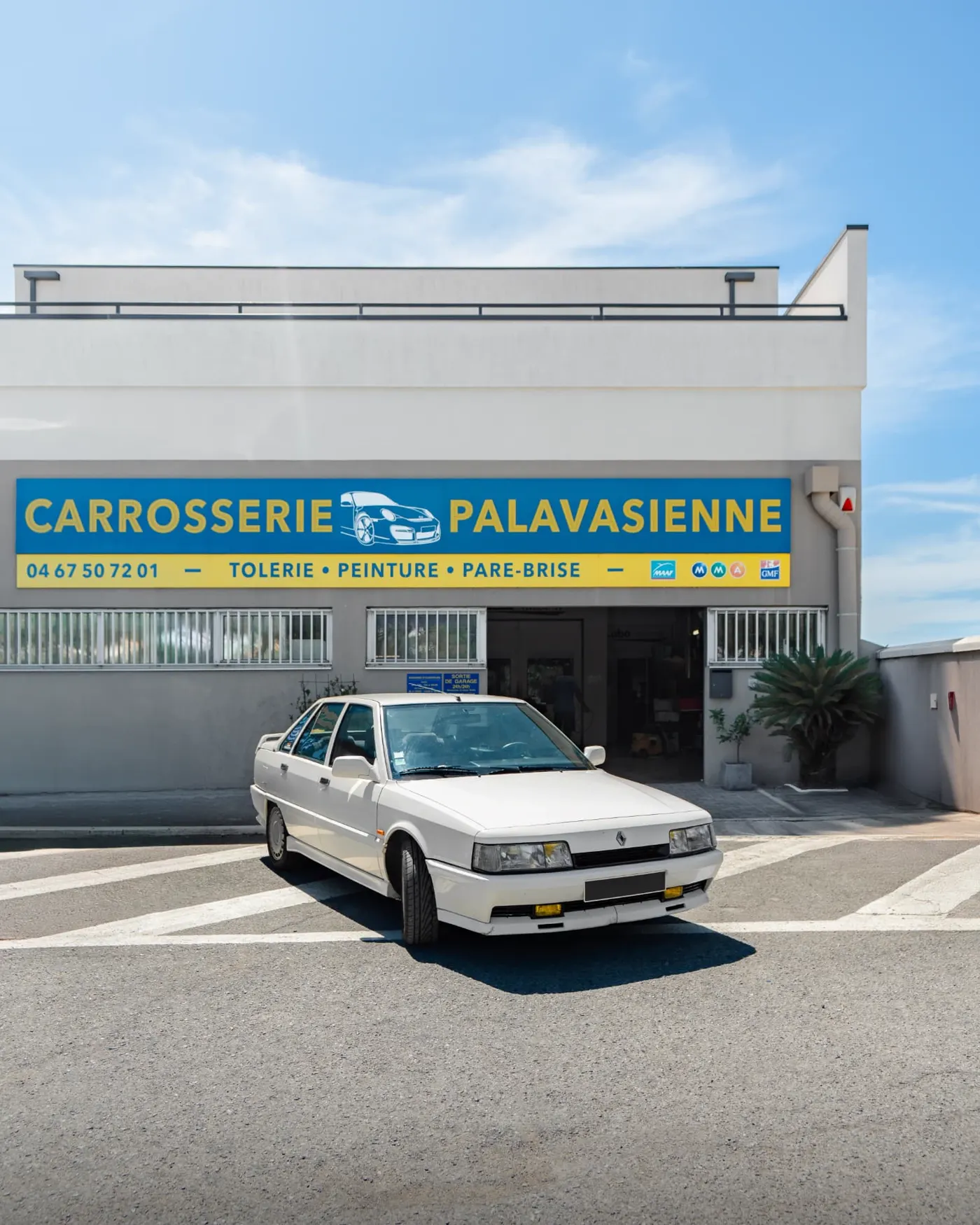Renault 21 blanche devant la facade d'une carrosserie