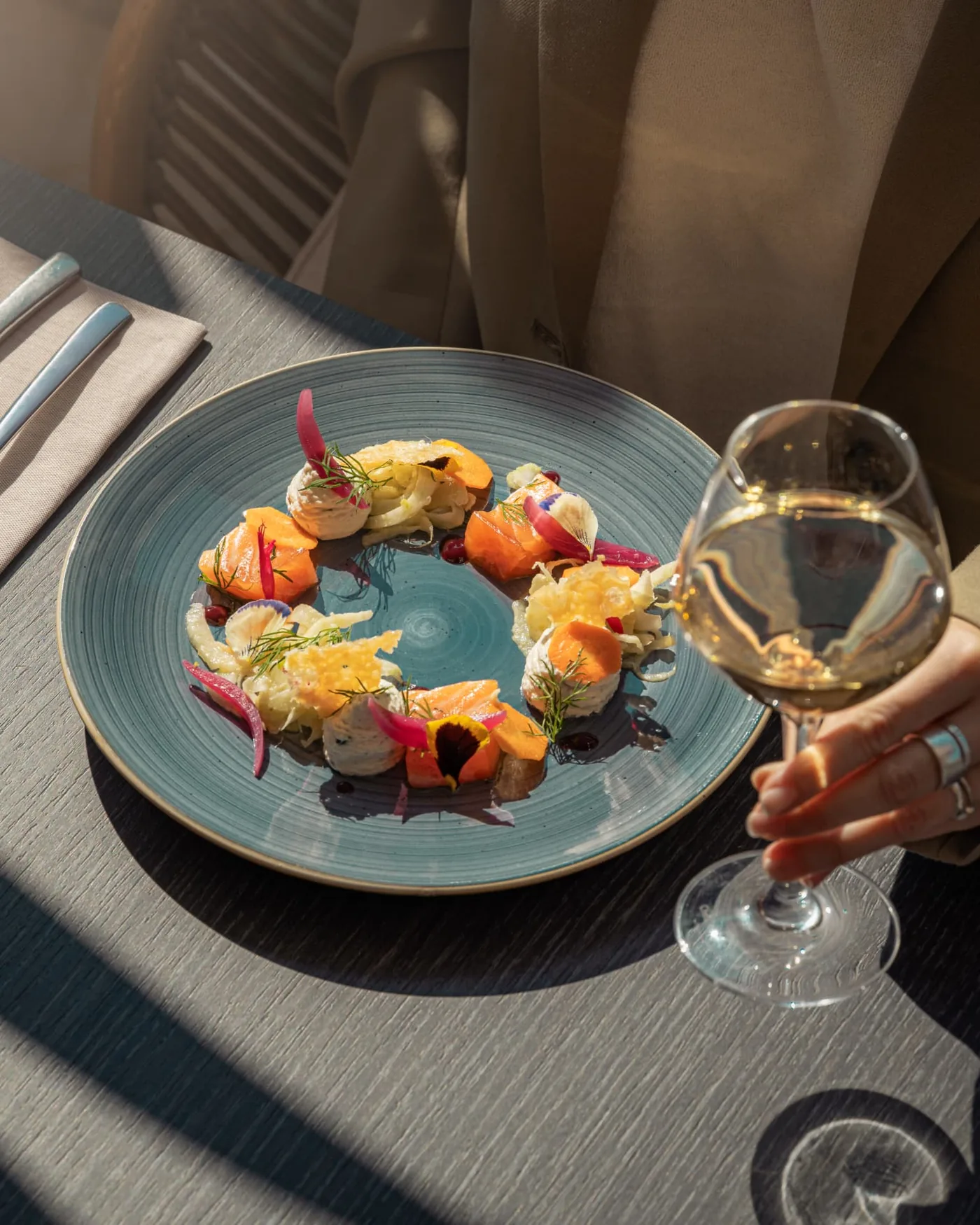 Entrée de saison dressée dans une assiette bleue, servie en terrasse avec un verre de vin blanc