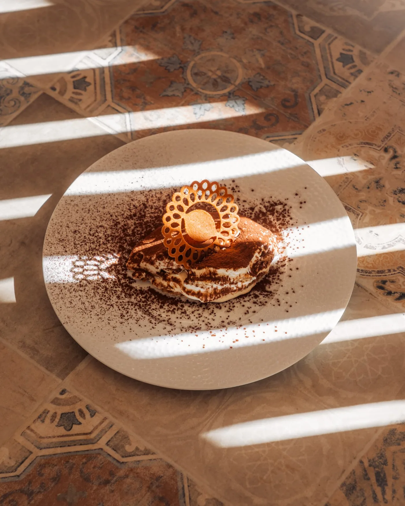 Dessert au cacao et tuile de sucre photographié en lumière rasante sur un sol en carreaux de ciment
