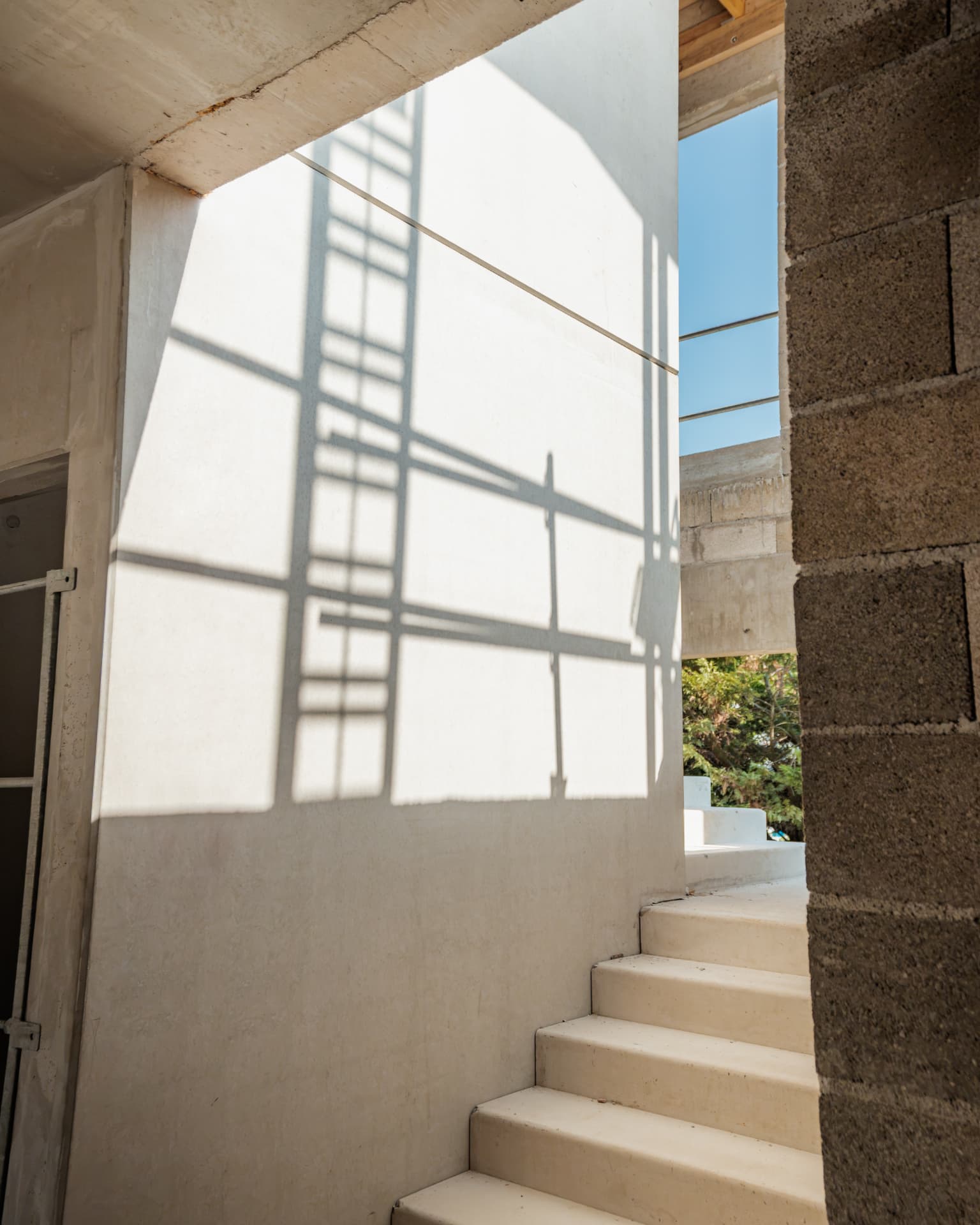 Escalier en béton d'une construction en cours, ombres d'échafaudage projetées sur un mur enduit