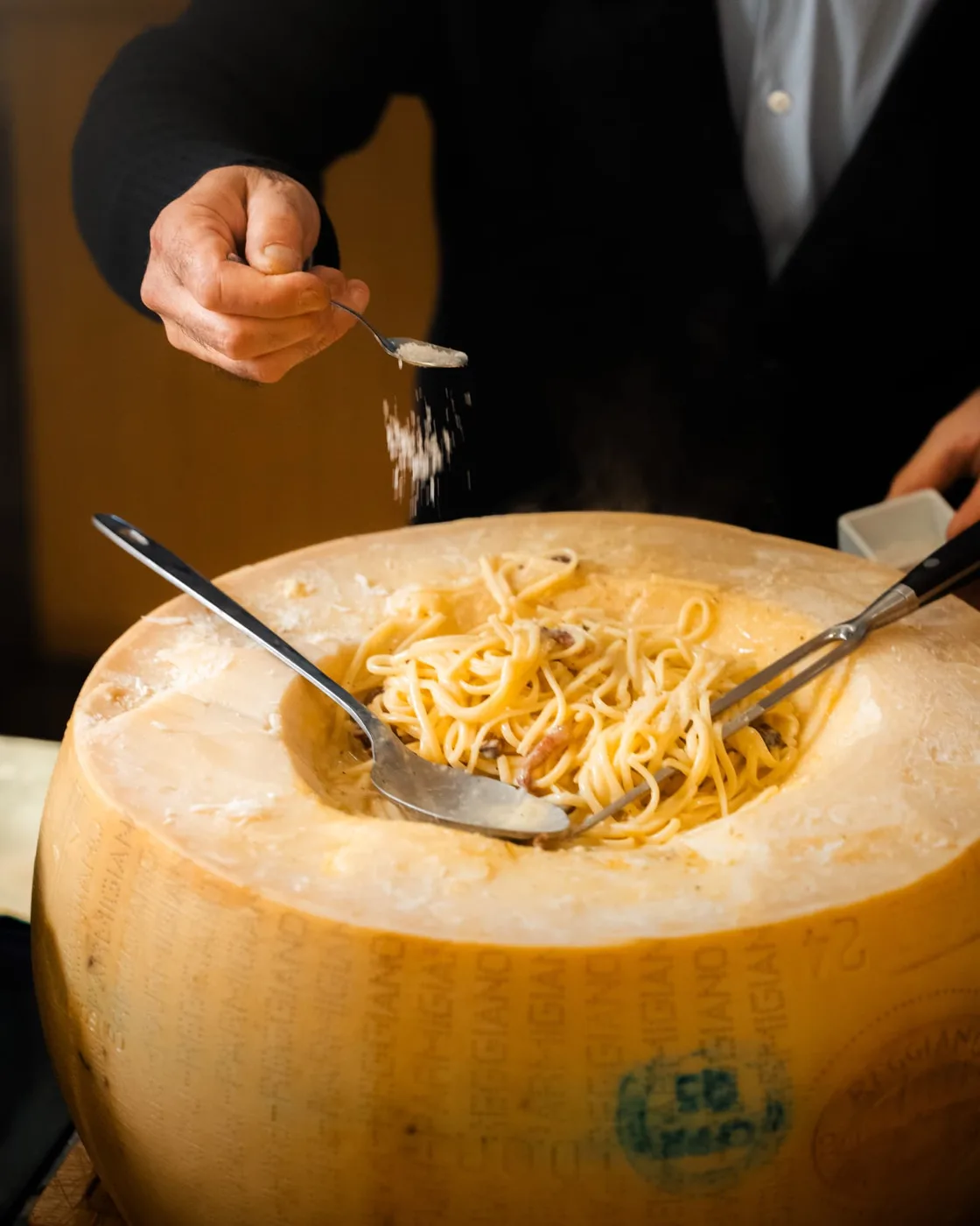 Râpé de parmesan au-dessus de spaghettis servis dans une meule de fromage, lors d'un service en restaurant