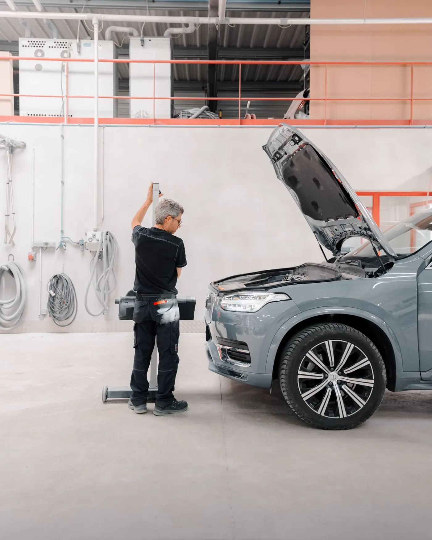 Technicien preparant un Volvo XC90 gris capot ouvert en atelier
