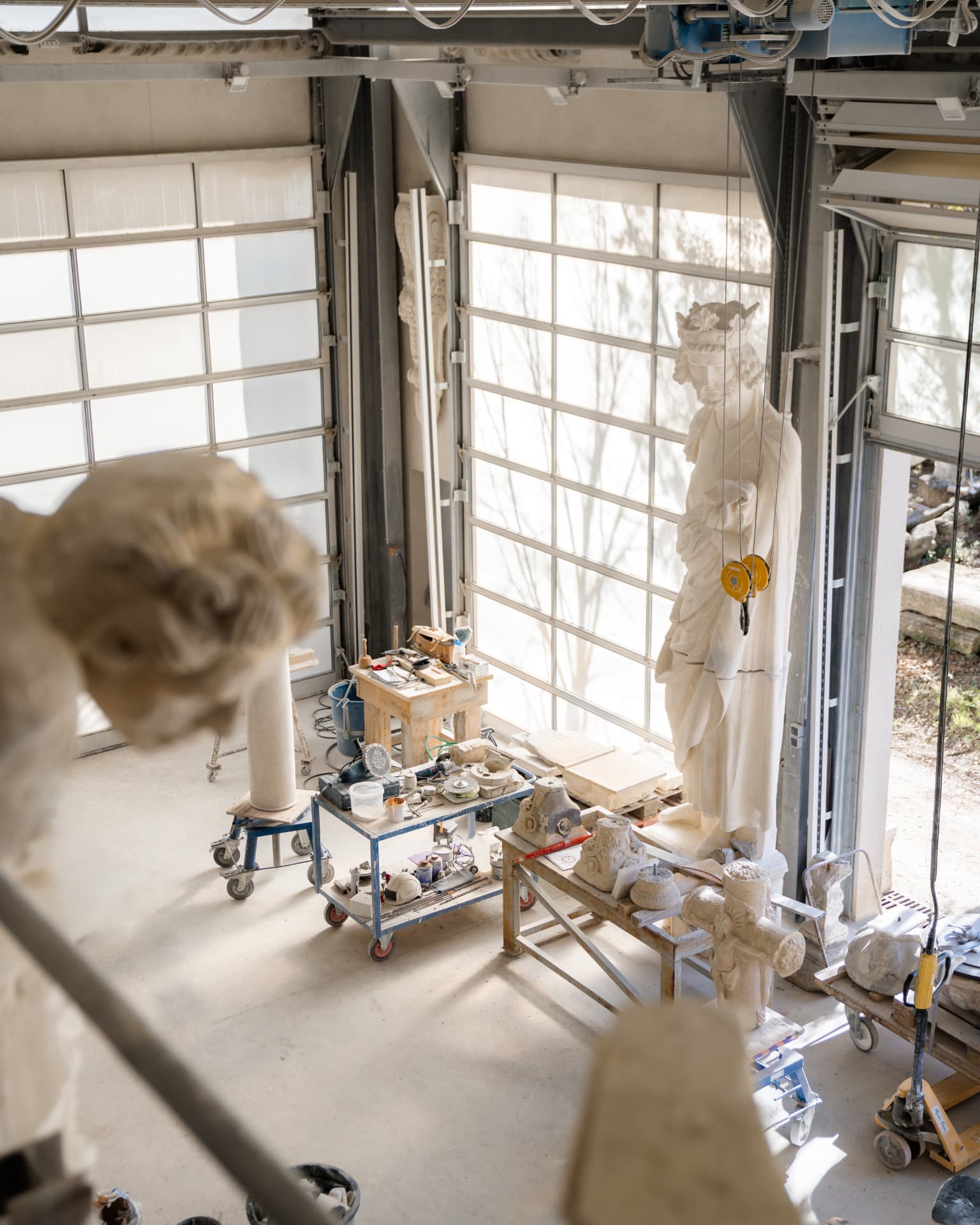 Vue en hauteur d'un atelier de taille de pierre, statue en cours de travail suspendue devant une grande verrière