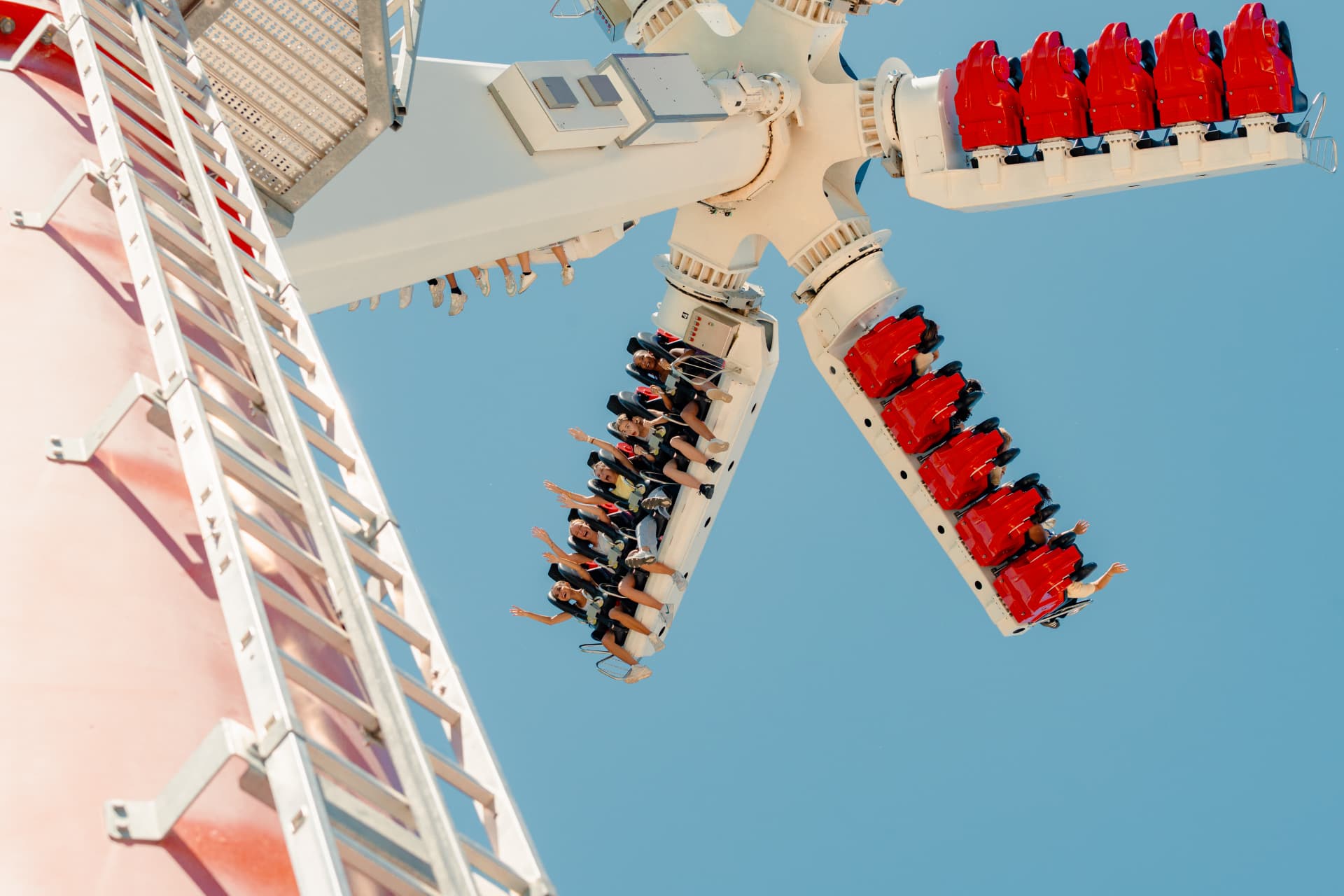Attraction à bras rotatifs vue en contre-plongée, nacelles rouges suspendues dans le ciel avec les visiteurs à bord