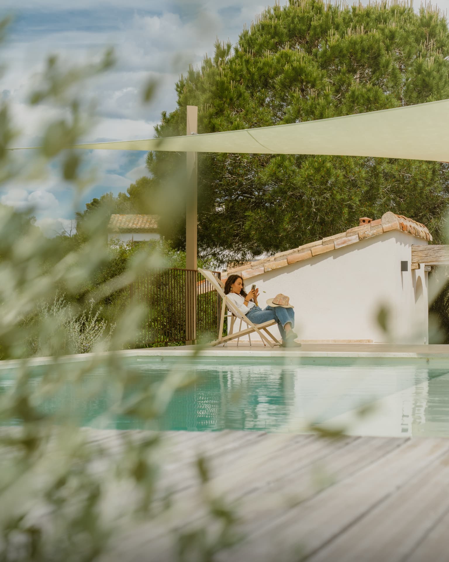 Voyageuse installée dans un transat au bord de la piscine d'un mas provençal, sous une voile d'ombrage