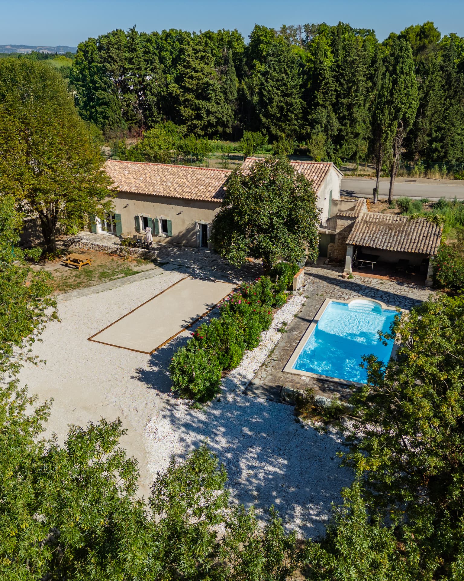 Vue aérienne d'un mas provençal entouré d'arbres, avec sa cour, son terrain de pétanque et sa piscine