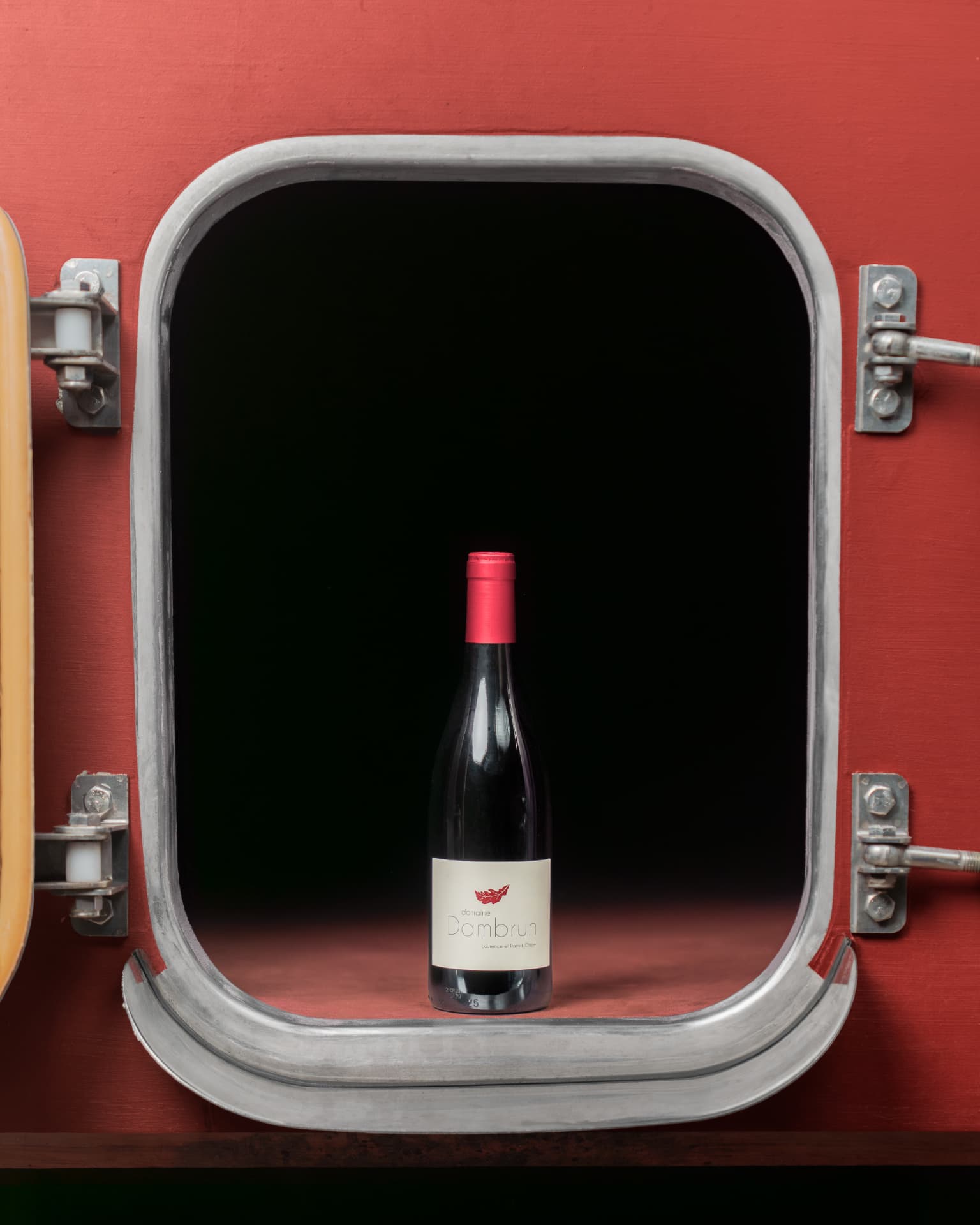 Bouteille de vin rouge présentée devant la porte ouverte d'une cuve de vinification peinte en rouge