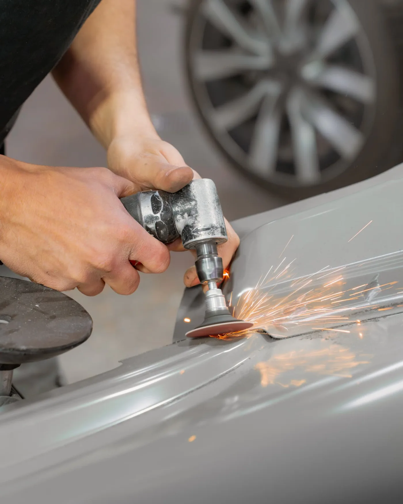 Gros plan sur un geste technique de carrosserie : ponçage d'un élément de véhicule, gerbe d'étincelles