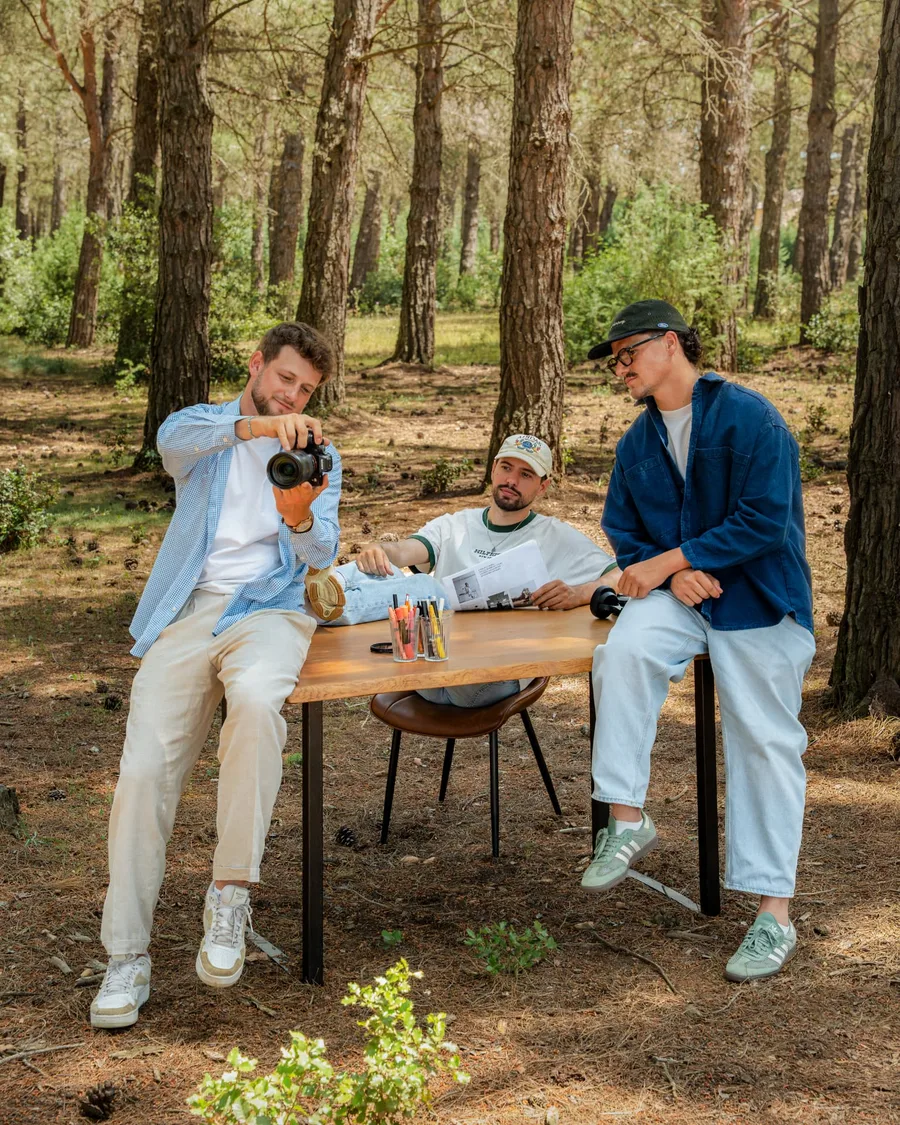 Trois photographes et vidéastes de BICPOM installés autour d'une table en pinède, un appareil photo à la main