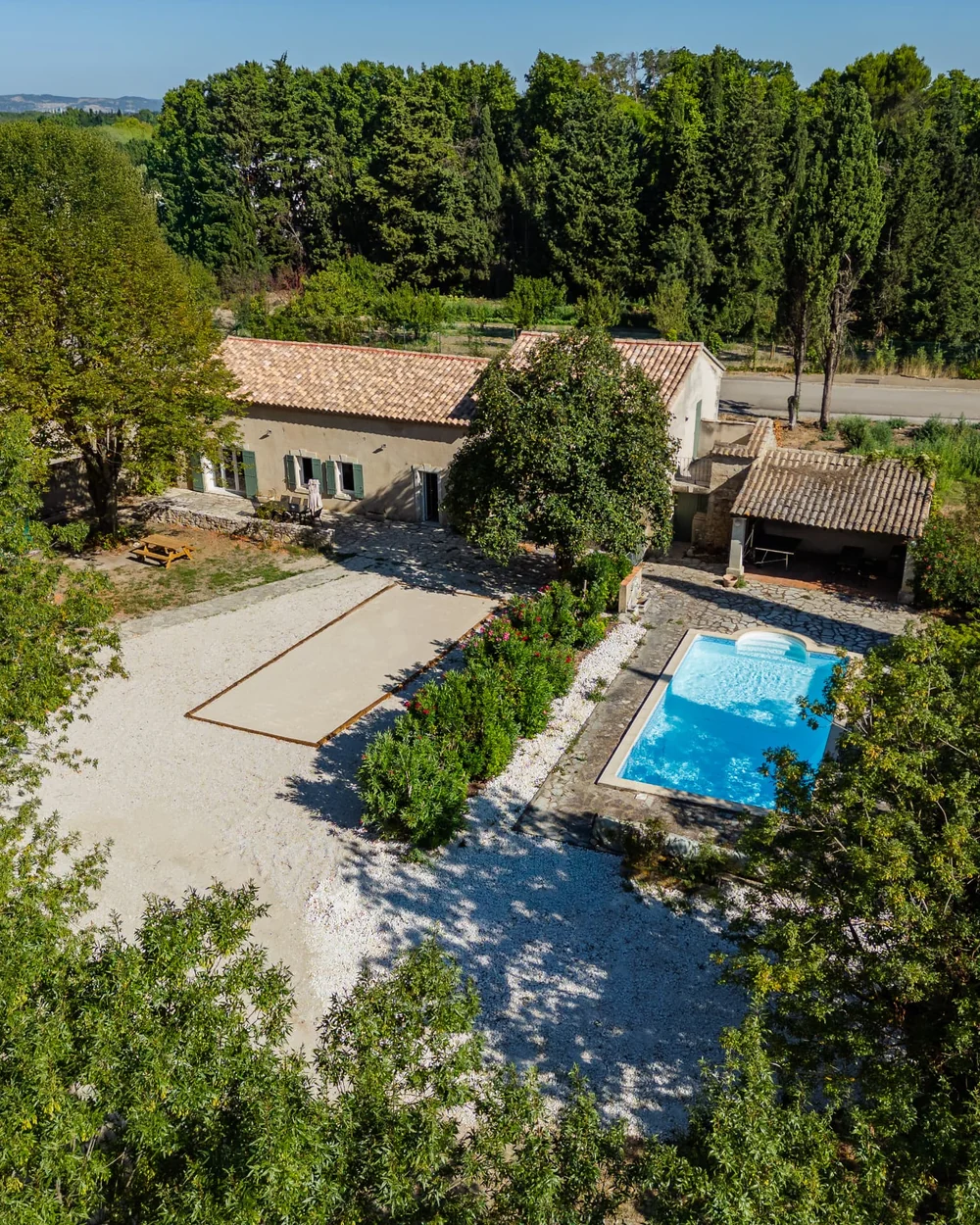 Vue aérienne du Mas de Valens : mas provençal en pierre, terrain de pétanque, piscine et pinède